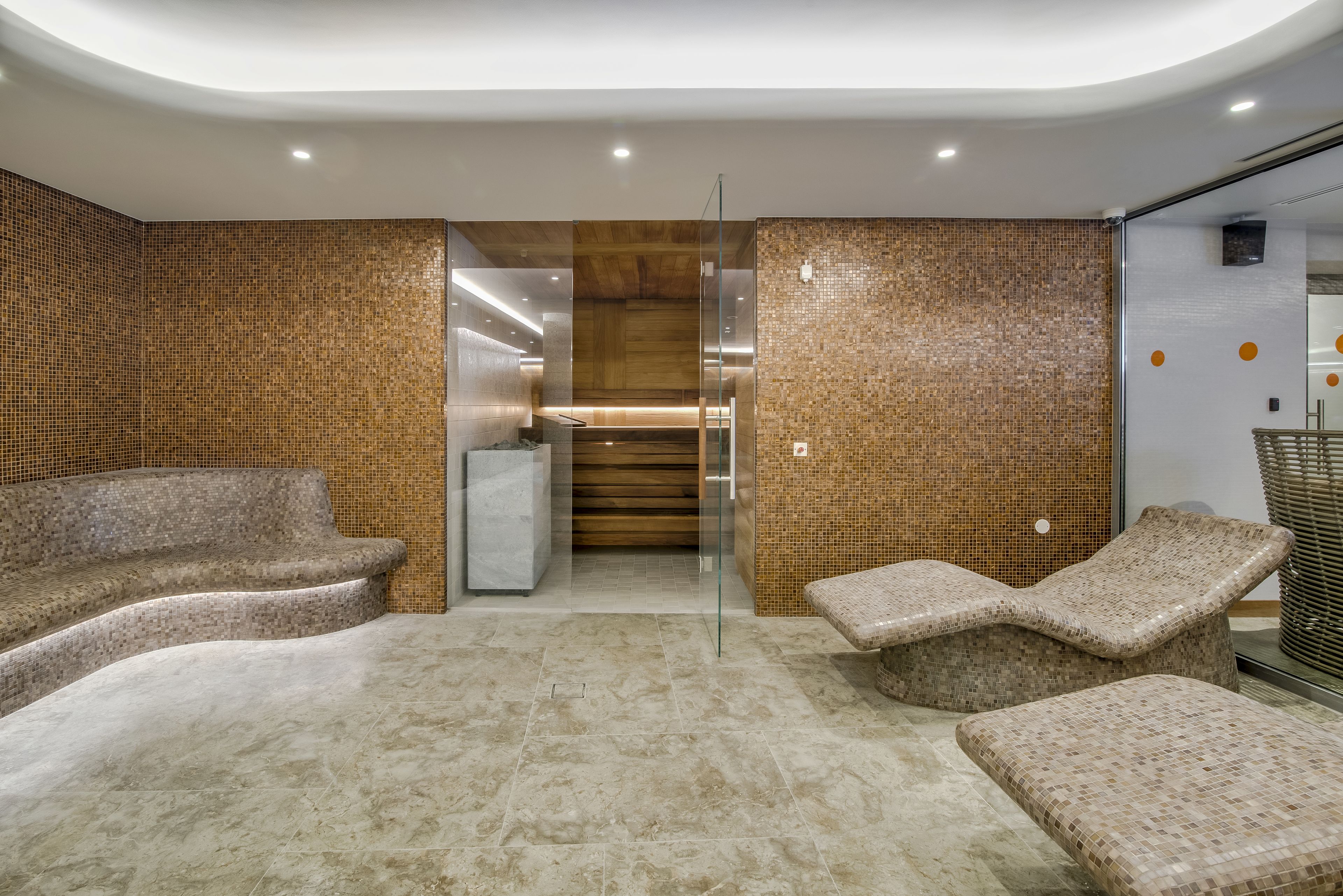 A modern spa area with mosaic tile walls, a central staircase, and lounge chairs.