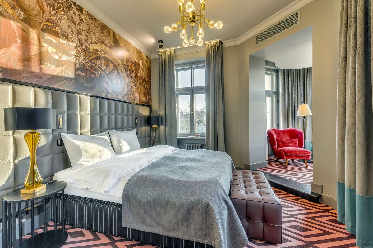 A modern hotel room with a large bed, a seating area, and a view of the outdoors.