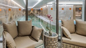 Un moderno espacio de spa con un jacuzzi envuelto en cristal, asientos acolchados y un jarrón decorativo.