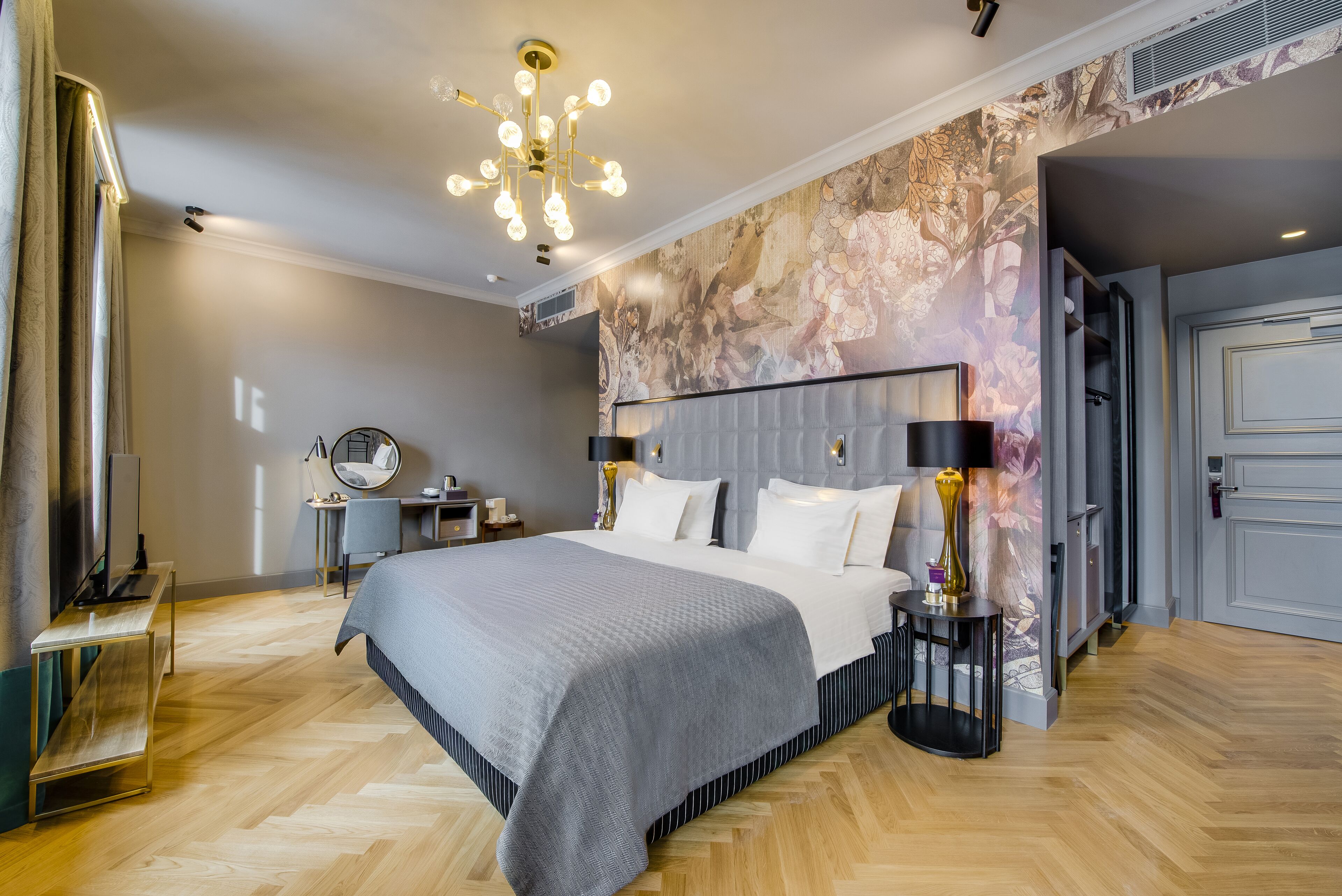 Un dormitorio moderno con una cama grande, una araña, un escritorio y un mural en la pared.