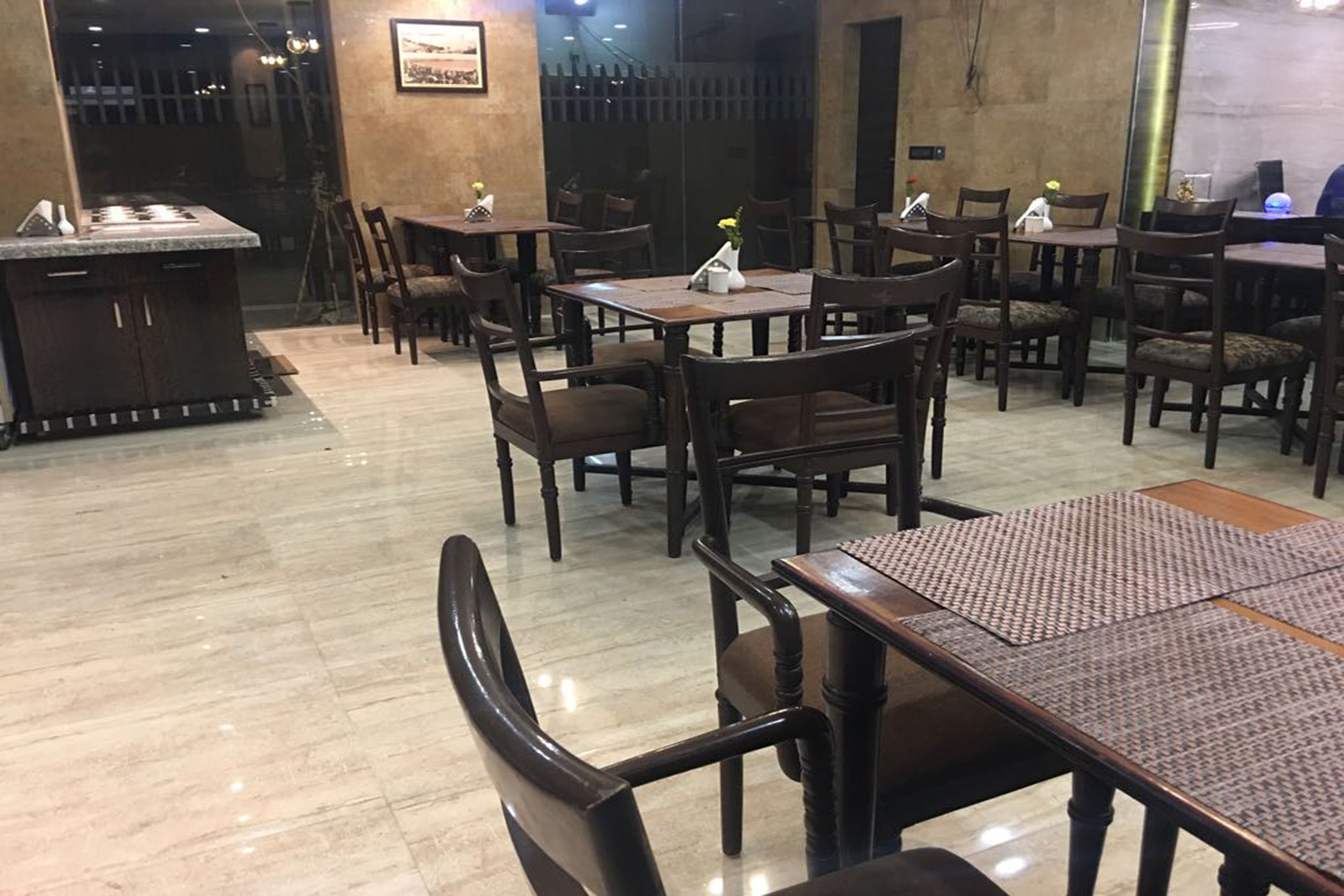 Un restaurante con mesas y sillas de madera, una zona de cocina y un suelo de baldosas.