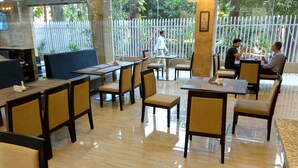 Un restaurante con varias mesas y sillas, piso limpio y una valla blanca al fondo.