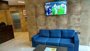 Un vestíbulo con un sofá azul, una mesa de centro de vidrio, una recepción y un televisor mostrando un evento deportivo.