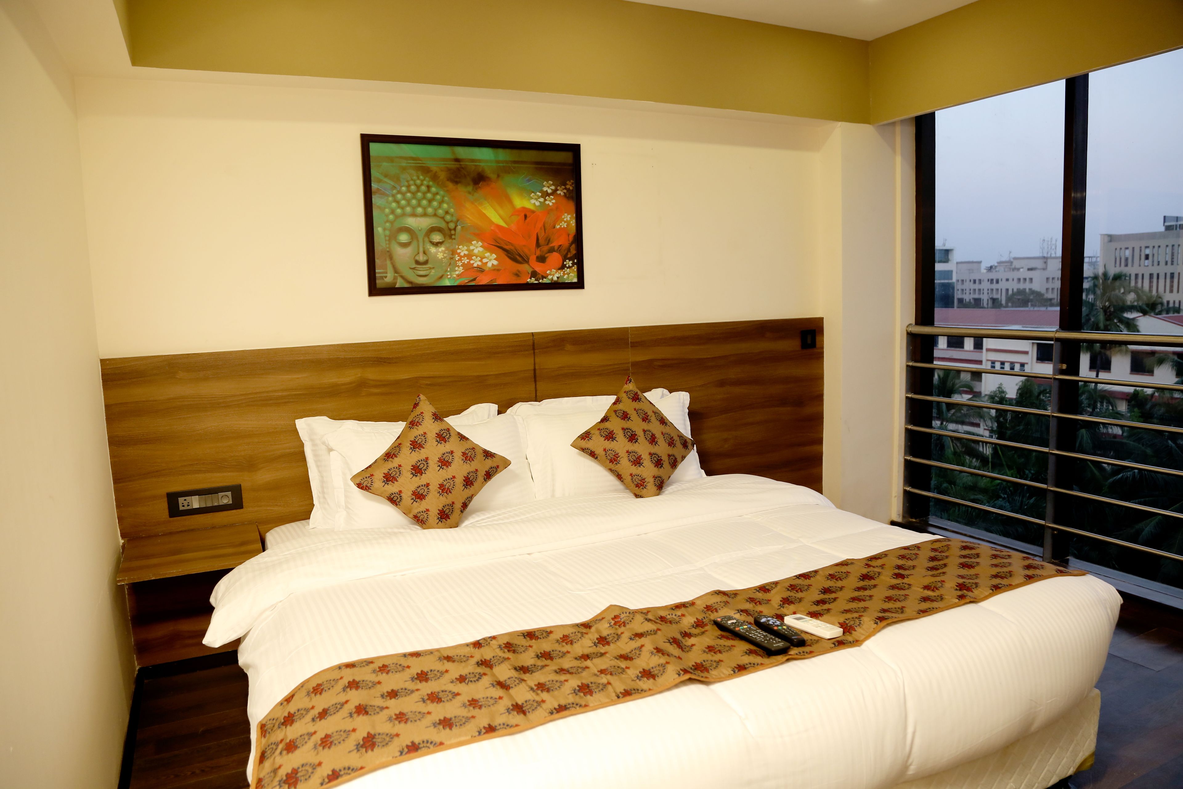 Habitación de hotel con una cama grande, cabecera de madera, un cuadro en la pared y vistas por la ventana.