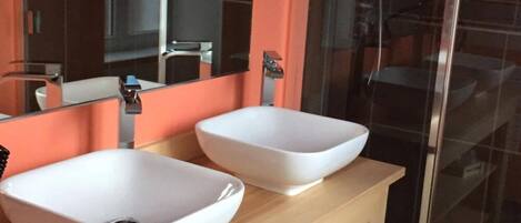A modern bathroom with two white sinks, a large mirror, and a glass shower enclosure.