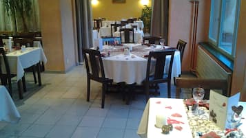A restaurant with multiple tables set for dining, featuring white tablecloths and dark wooden chairs.