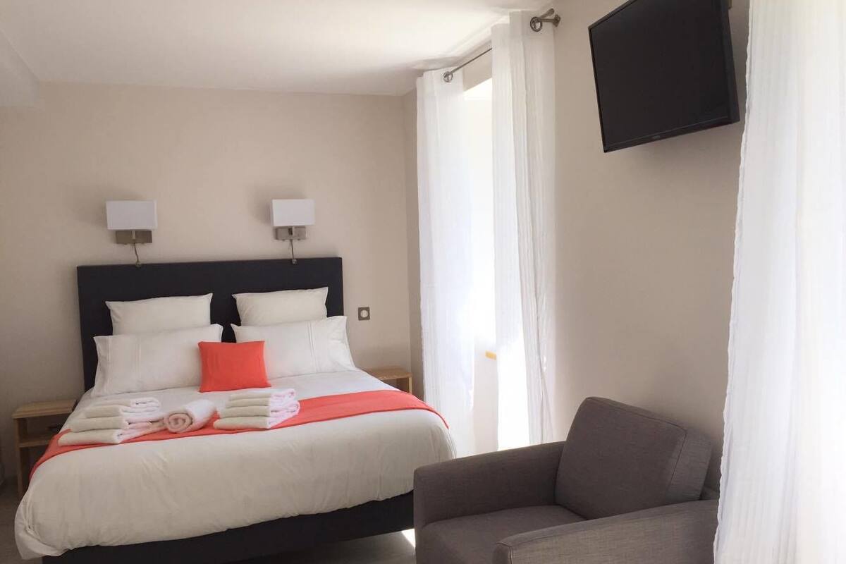 Une chambre d’hôtel avec un lit, une chaise, une télévision et des rideaux.