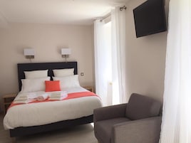 Una habitación de hotel con cama, una silla, televisor y cortinas.