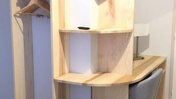 A compact room with a built-in wooden desk, a grey upholstered bench, and a clothing rack.
