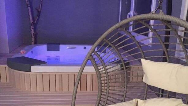 Un bain à remous avec une terrasse en bois et un fauteuil en osier.