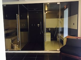 Un baño moderno con cabina de ducha de vidrio, un banco de madera y un inodoro a la vista.