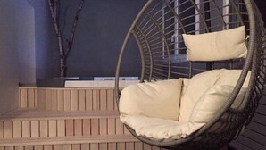 Un fauteuil suspendu avec des coussins, dans une pièce aux murs lambrés et à un mur de couleur sombre.