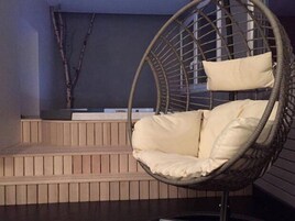 Una silla colgante con cojines en una habitación con paneles de madera y una pared oscura.