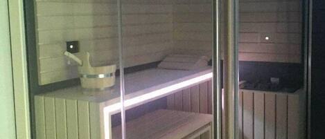 Una sauna con un banco de madera, una mesita con un balde y un reloj en la pared.