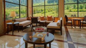 A spacious living area with a large window offering a view of a lush green landscape and mountains. There is a sofa, chairs, a small table with a vase, and a lamp. - The Sultan Resort (Gund)