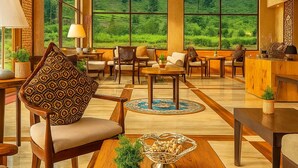 A spacious room with a large window offering a view of a lush green landscape. There are several wooden chairs and tables arranged for dining or relaxation. - The Sultan Resort (Gund)