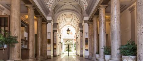 A grand hallway with tall columns, a patterned floor, and a chandelier.