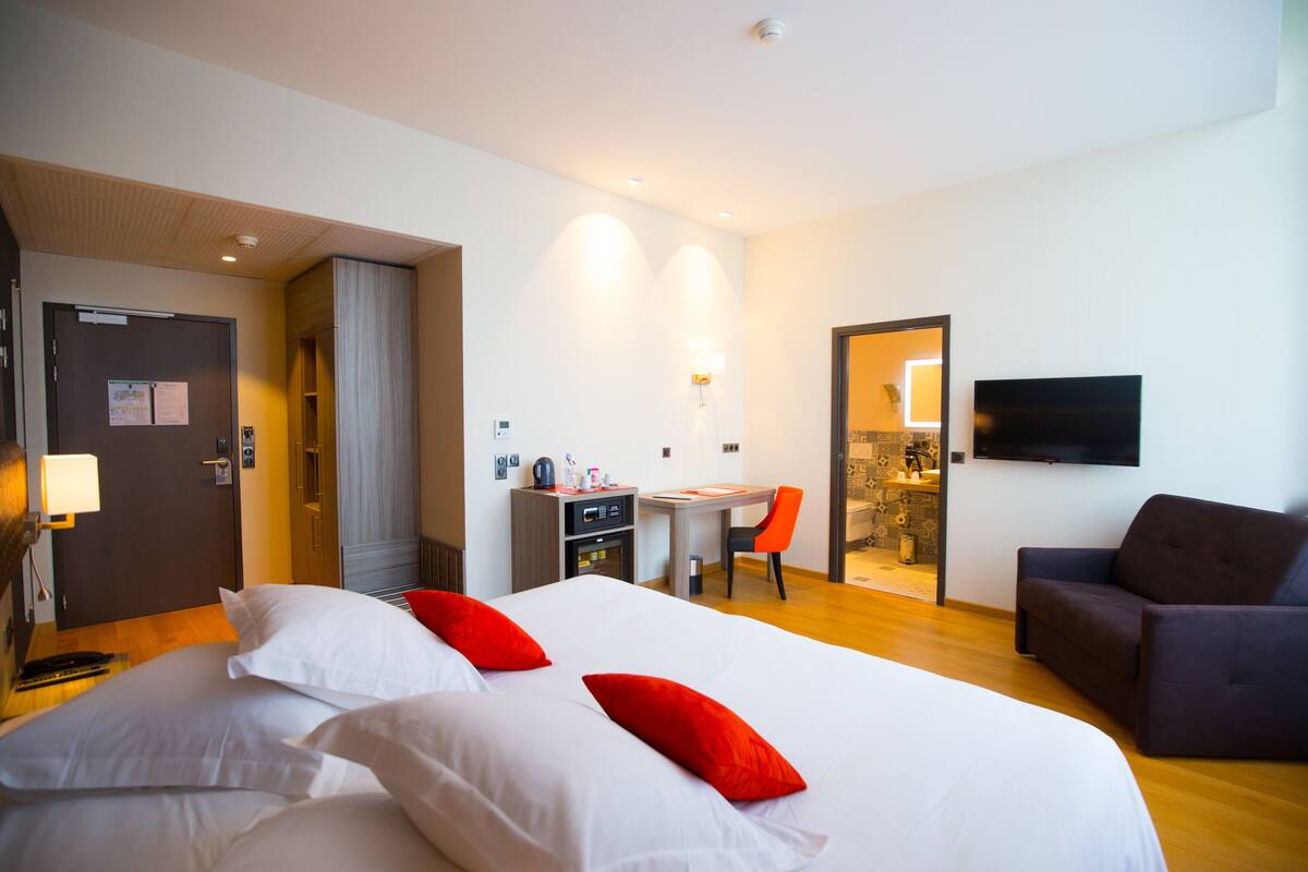 Ein Hotelzimmer mit Bett, Schreibtisch, Sessel, Sofa und Fernseher.