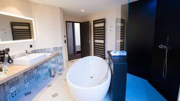A modern bathroom with a freestanding bathtub, a large mirror, and a dark shower area.