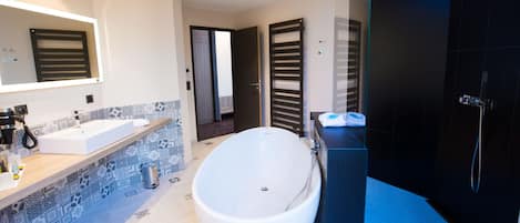 Un baño moderno con una bañera independiente, un espejo grande y una zona de ducha oscura.