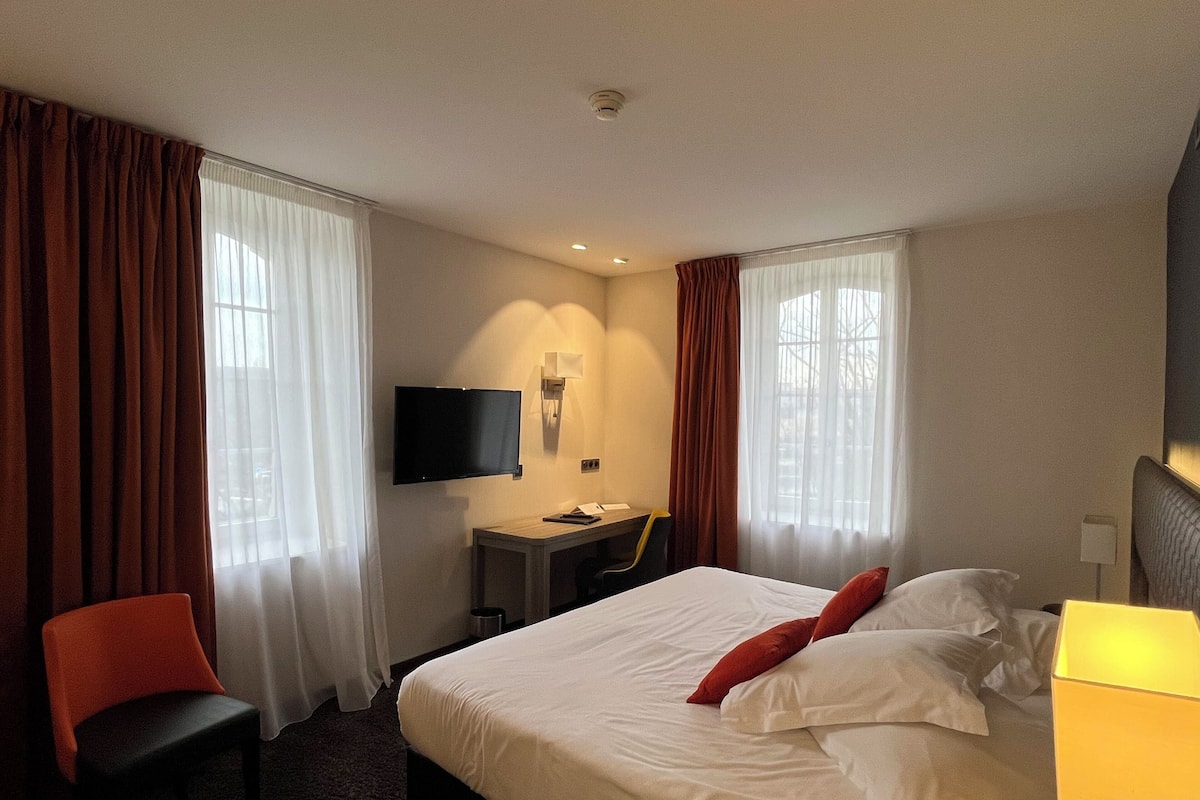 Ein Hotelzimmer mit Bett, Schreibtisch mit Stuhl, Fernseher und Vorhängen.