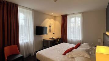 A hotel room with a bed, a desk with a chair, a television, and curtains.