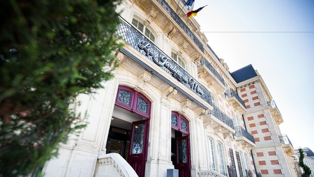 A historic building with ornate architectural details, including a grand entrance with red doors and a balcony with metal railings.