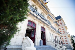 A historic building with ornate architectural details, including a grand entrance with red doors and a balcony with metal railings. - Les Jardins du Mess (Verdun)