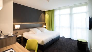 A hotel room with a large bed, a desk with a chair, a TV, and a window with curtains.