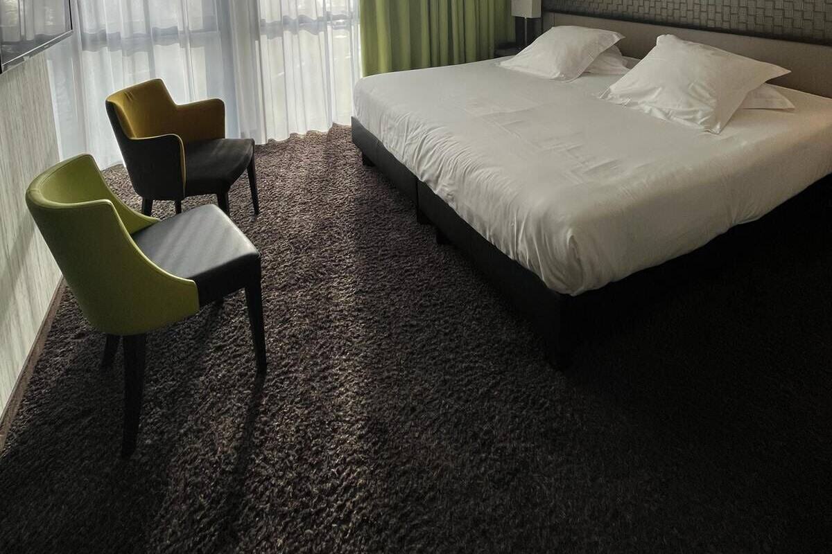 Ein Hotelzimmer mit einem großen Bett, zwei Sesseln, einem Fernseher und einem Fenster mit Vorhängen.