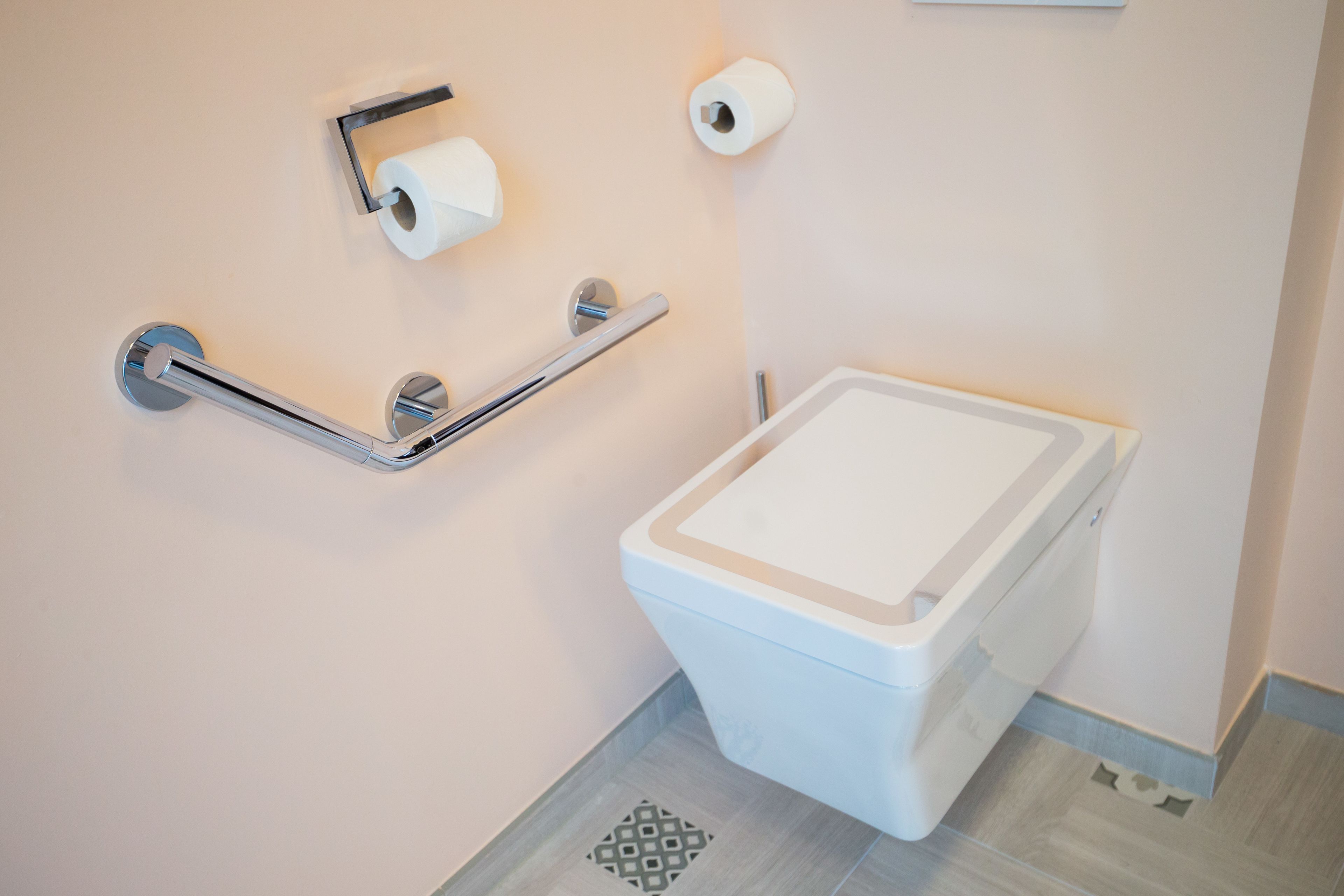 A modern bathroom with a toilet, grab bars, and toilet paper.