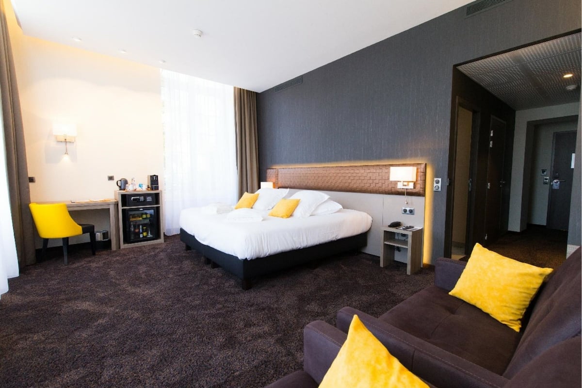 Ein Hotelzimmer mit einem großen Bett, einem Schreibtisch mit Stuhl, einer Couch und einem kleinen Tisch mit Lampe.