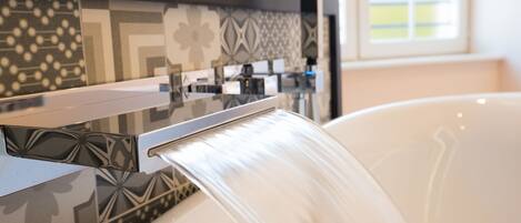 A bathroom with a modern sink, a faucet, and a bathtub with water flowing into it.