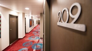 A hotel hallway with a red carpet, numbered doors, and a wall-mounted sign indicating room number 209.