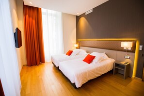 A hotel room with two beds, a nightstand, a lamp, and a window with curtains.