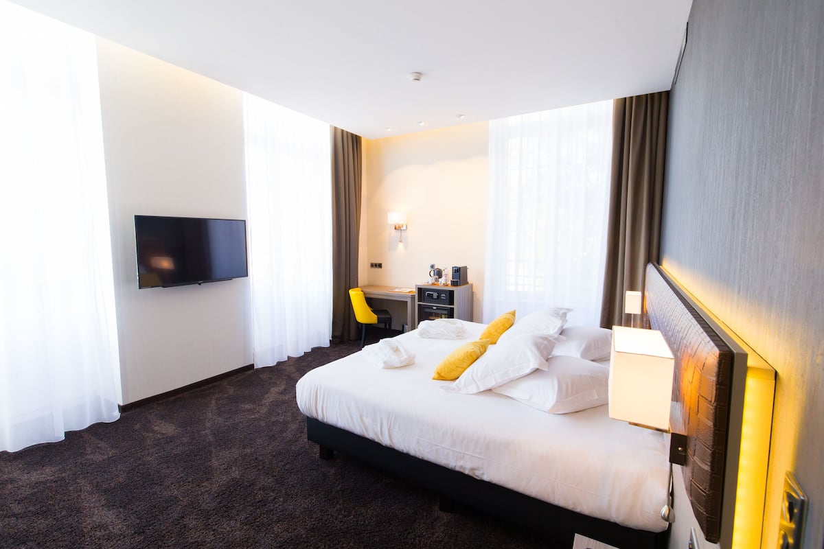 Ein Hotelzimmer mit einem großen Bett, einem Schreibtisch, einem Stuhl, einem Flachbildfernseher und einer Lampe.