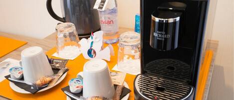 Una estación de café con cafetera, tazas, hervidor y una botella de agua.