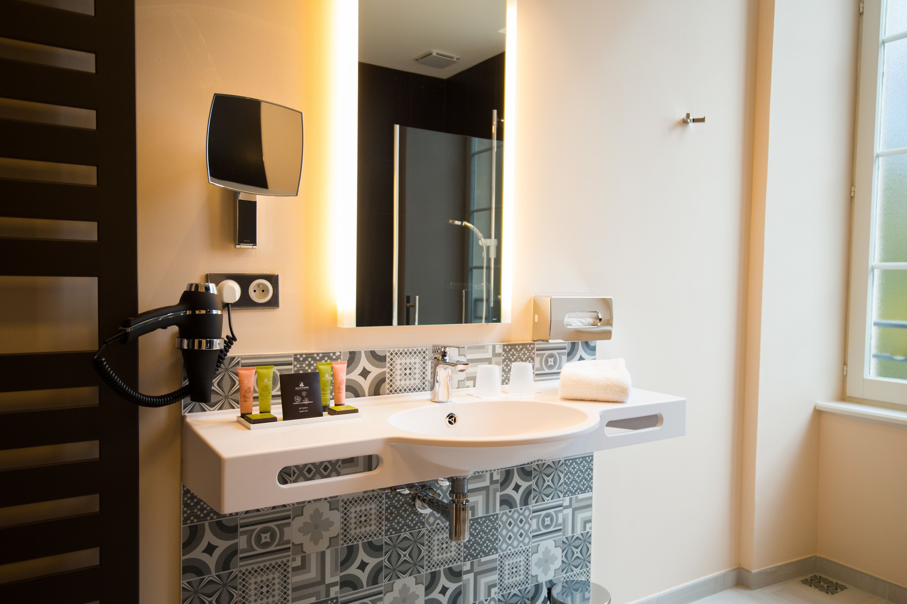 Een moderne badkamer met een grote spiegel, een haardroger en een wastafel met toiletartikelen.