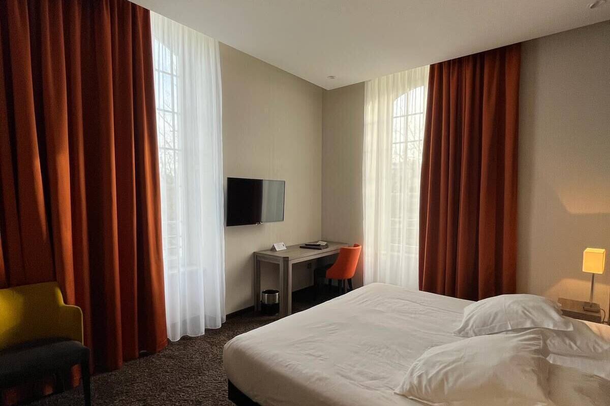 Ein Hotelzimmer mit einem großen Bett, einem Schreibtisch mit Stuhl, einem Fernseher und Vorhängen.