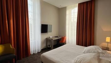 A hotel room with a large bed, a desk with a chair, a television, and curtains.