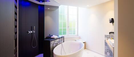 A modern bathroom with a freestanding bathtub, a shower enclosure, and a window providing natural light.
