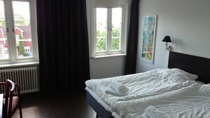 Une chambre d’hôtel avec un lit, une chaise, une fenêtre avec des rideaux et un radiateur.