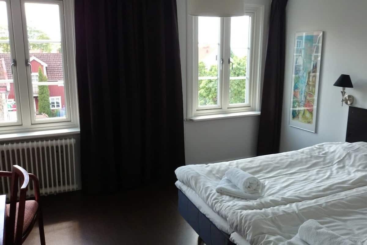 Una habitación de hotel con cama, una silla, ventana con cortinas y un radiador.