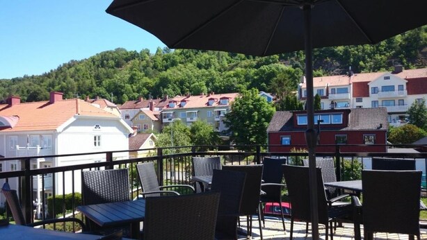 Une terrasse dotée de chaises et d’une table en osier, offrant une vue sur une colline parsemée de bâtiments résidentiels.