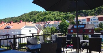 Una terraza con sillas de mimbre y una mesa, con vistas a una ladera con edificios residenciales.