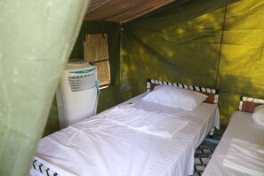 Una cama individual con ropa de cama blanca en una estructura tipo tienda con pared verde y una ventana.