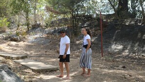 Two people standing on a dirt path with rocks and sparse vegetation.