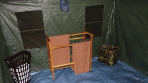 A tent with a wooden bench, a camouflage bag, and a laundry basket.