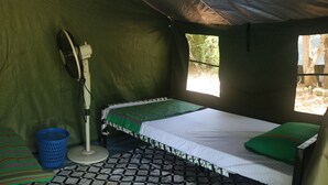 A tent with a bed, a fan, and a blue basket.