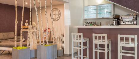 A modern kitchen with a bar area, white bar stools, and a clock on the wall.